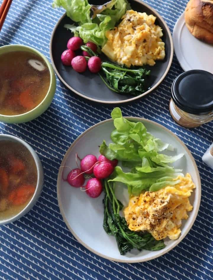 青い柄のテーブルクロスの上に皿とスープが置かれた朝食のテーブル