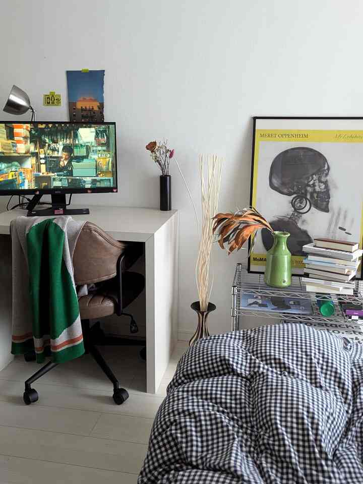 Bright white bedroom featuring black and white gingham bedding, a desk with office chair and monitor on the left, creating a cozy home cinema setup