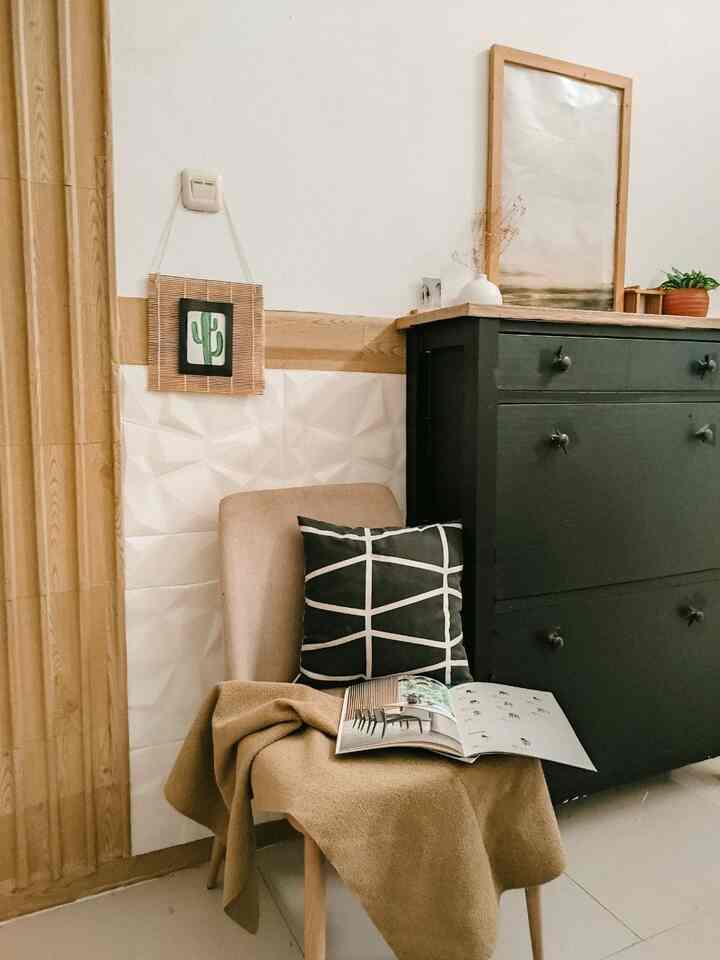 Natural tone wood wall panels and a black buffet cabinet in an entrance living room space, with a beige blanket and black cushion creating a cozy atmosphere.