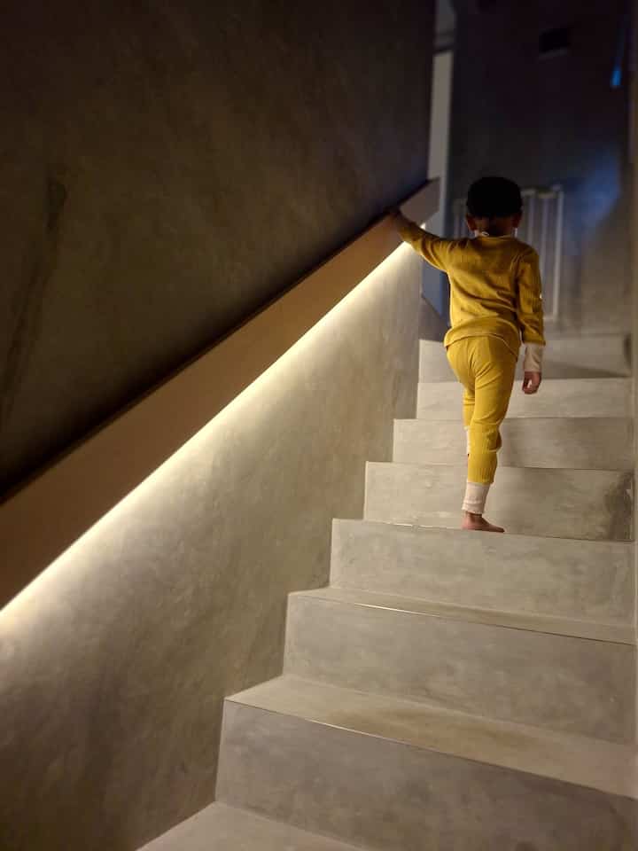 Natural-tone concrete stairs and walls with LED wall lighting, featuring a child safely navigating the stairway in a cozy interior