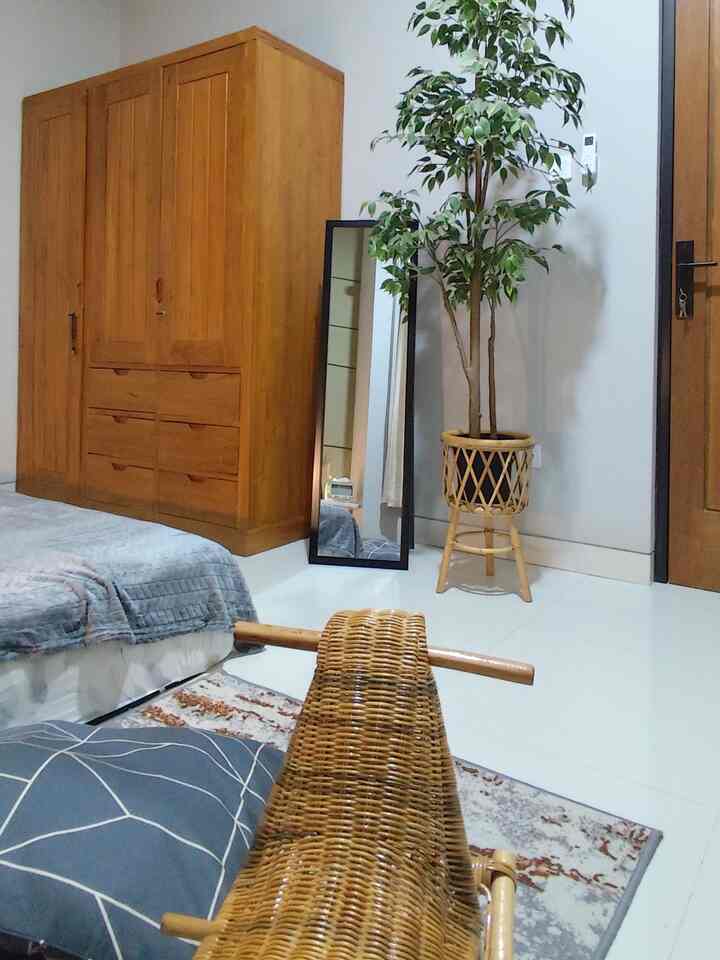 Natural-colored bedroom featuring large wooden wardrobe, rattan plant pot, and full-length mirror in a cozy setting