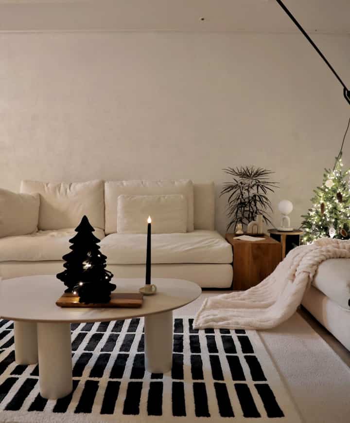 White and black toned living room featuring cream sofa, oval coffee table, mini Christmas tree, and warm lighting in a modern setting
