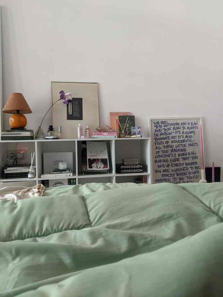 Natural-toned bedroom of about 6 tatami mats with white walls and shelves, featuring green bedding and an orange table lamp