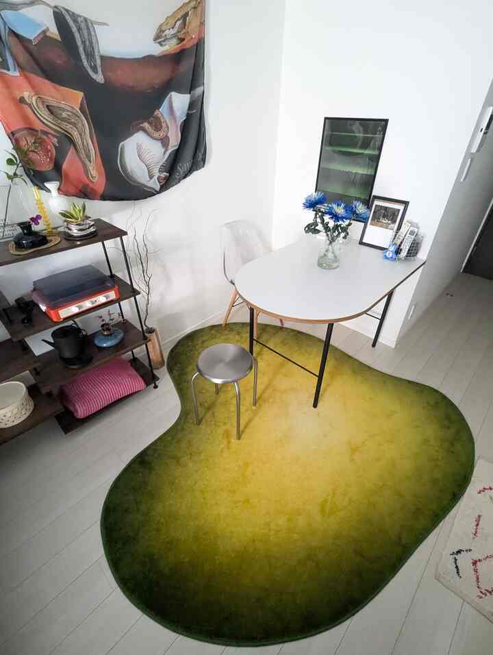 緑と黄色のグラデーションラグの上に白いテーブルと銀色のスツールが配置された、植物とポスターがアクセントのナチュラルなダイニングルーム