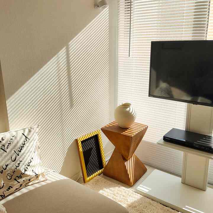 アイボリーと木目調の1K一人暮らしリビング、木製スツールのサイドテーブルと花瓶が配置された雰囲気のある北欧インテリア