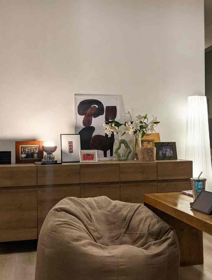 Natural-toned living room featuring beige bean bag, wooden dresser, and table lamp creating a cozy atmosphere