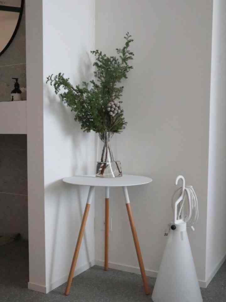 白い壁に囲まれた玄関、自然な木目調の脚を持つ白い丸テーブルの上にモミの枝が活けられた花瓶が置かれたシンプルなインテリア