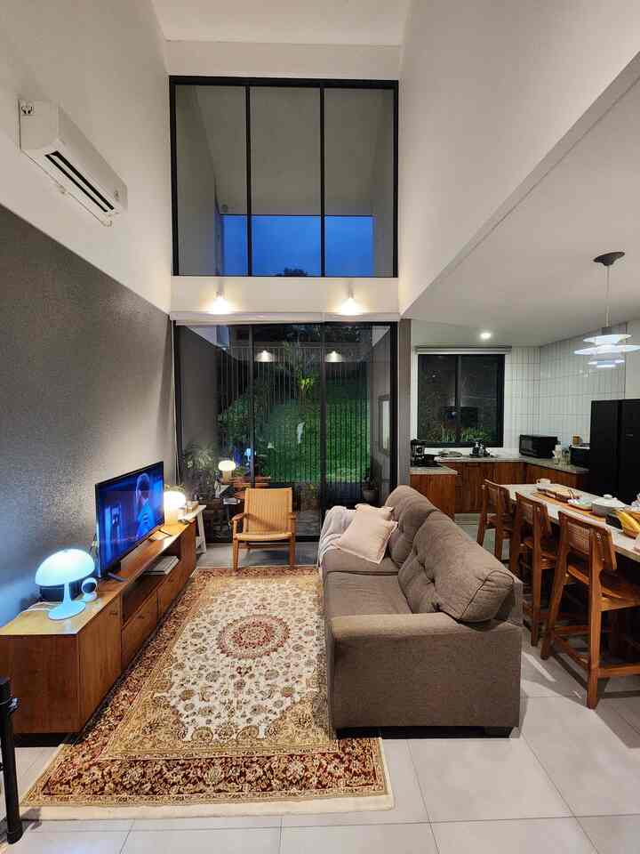 Natural modern living room with gray sofa and wooden furniture, cozy space featuring large glass doors revealing night scenery