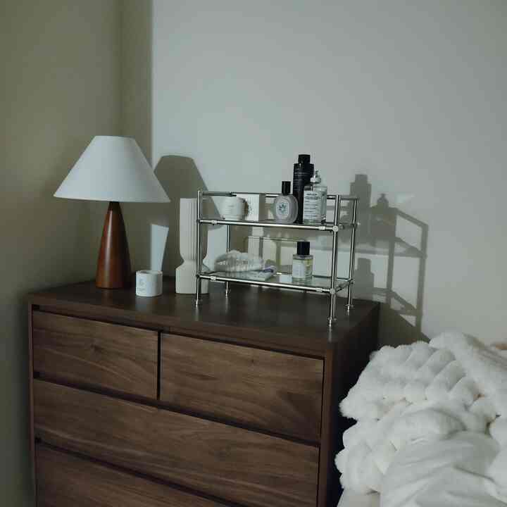 ブラウンのチェストとステンレス製の棚が配置されたナチュラルモダンな寝室の落ち着いた雰囲気のあるインテリア