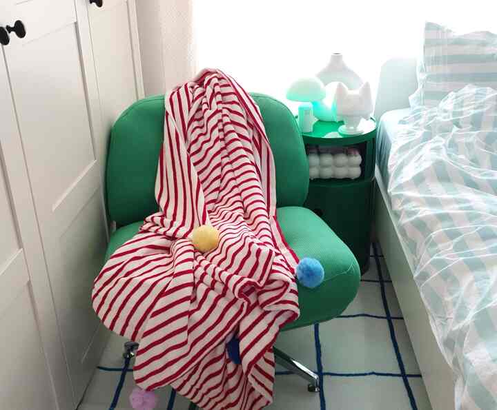 明るいホワイトとグリーンのトーンの寝室、ミッドセンチュリーモダン風のグリーンのアームチェアとストライプ柄の布団カバーが配置された雰囲気のあるインテリア