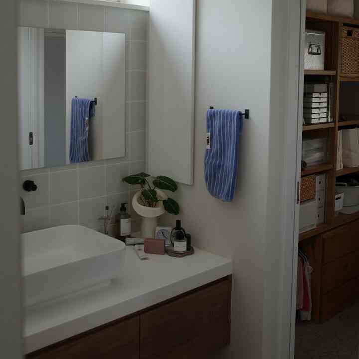 白とブラウンのトーンのバスルーム、白い洗面台と青のストライプタオルが整然と配置された落ち着いた雰囲気のインテリア