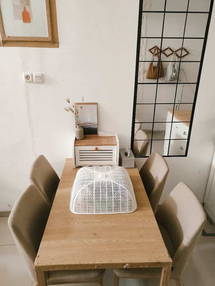 White-walled dining room featuring a wood-tone table with four beige dining chairs in a minimal, warm setting