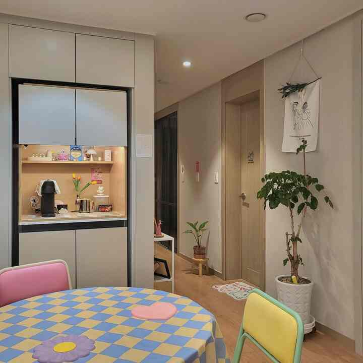 Pastel-toned dining room and kitchen with a colorful dining table and chairs, featuring natural plants that add warmth to the space