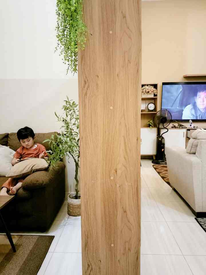 Beige and brown toned living room featuring sofas, a central wooden pillar, and an artificial olive tree creating a natural family space