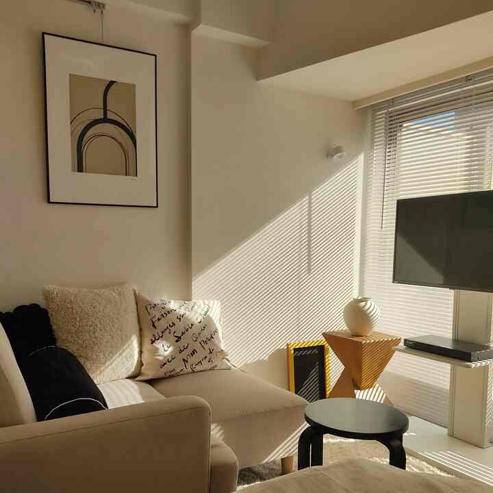 Beige and white toned single household living room featuring a beige sofa and wooden side table bathed in warm sunlight