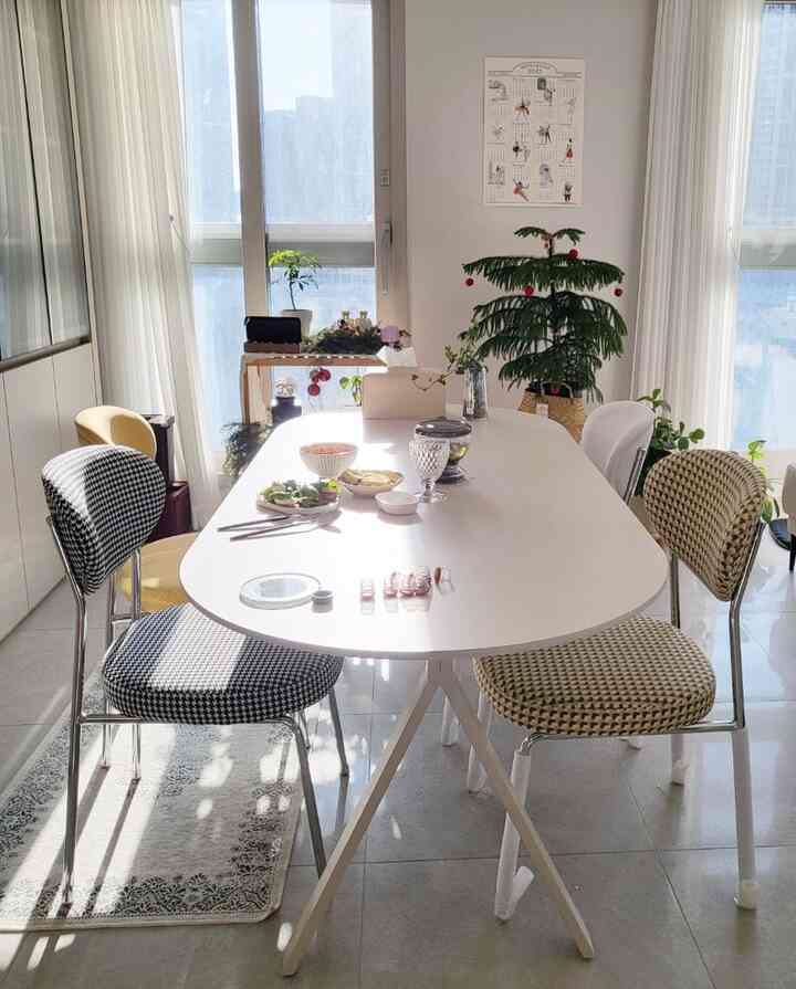 White and beige toned dining room featuring an oval dining table, patterned dining chairs, and green plants by the window creating a calming atmosphere