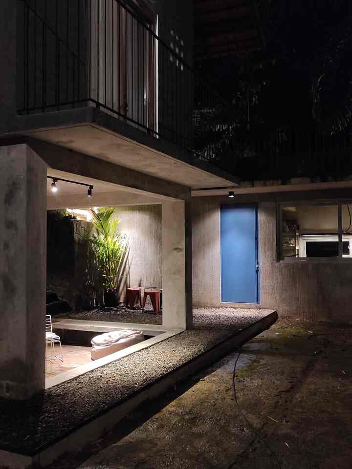 Light gray concrete home office area with blue door, featuring a bean bag and outdoor chair in a calm semi-outdoor nighttime setting