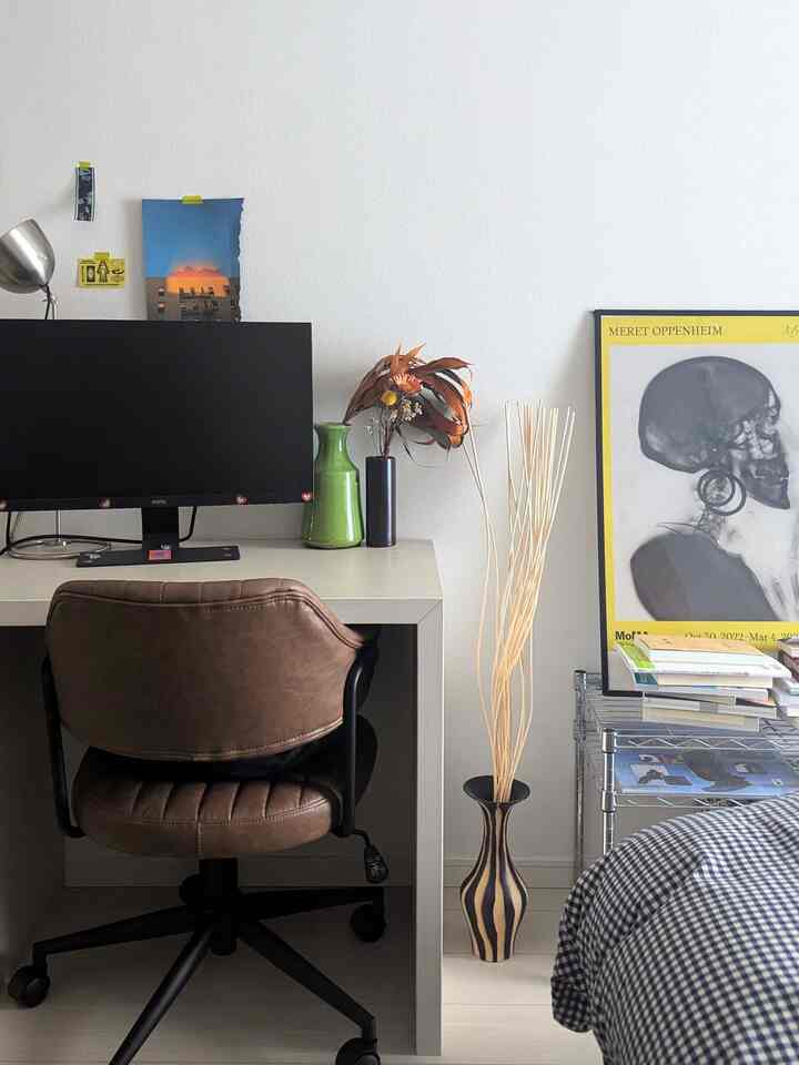 白い壁とブラウンのレザー椅子、モニターと花瓶が配置されたシンプルなホームオフィス空間