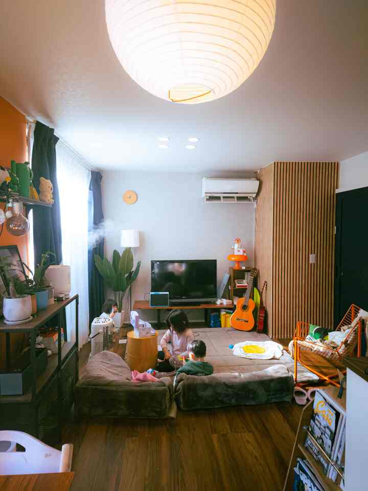 Light gray walled living room with dark brown wooden floor, featuring children and scattered furniture items creating a casual atmosphere