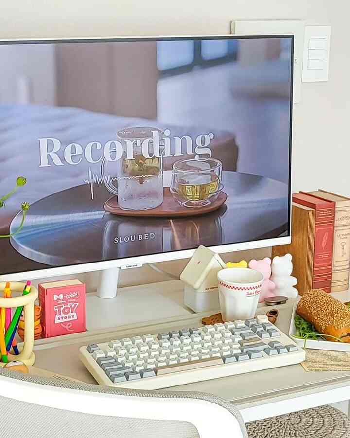 White-toned home office space featuring a monitor and keyboard on a neat desk with beverages and books creating a cozy work area