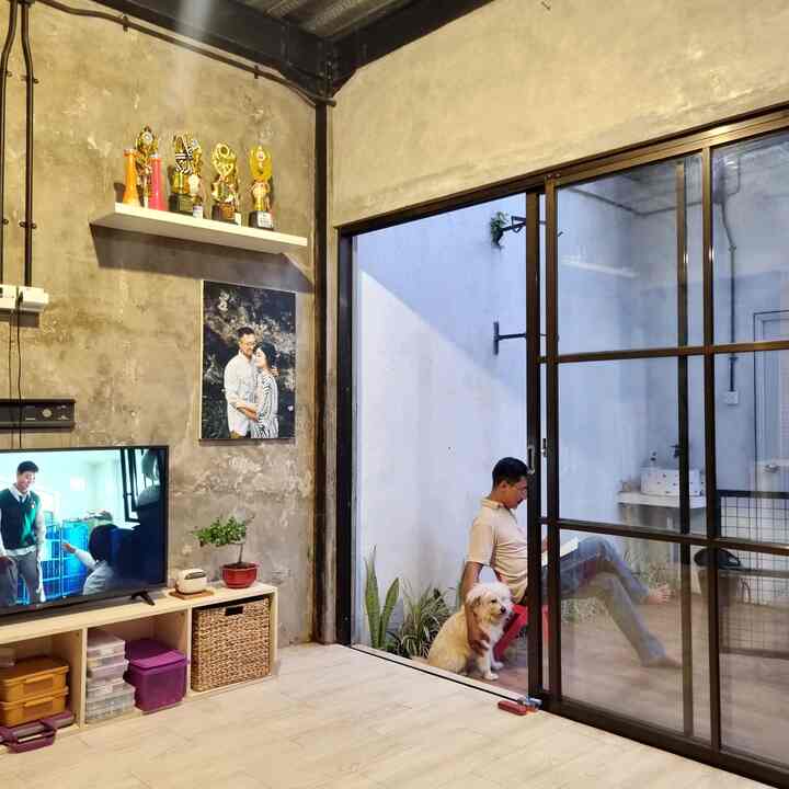 Natural-toned living room and balcony space with concrete walls, featuring a man sitting with a dog creating a cozy atmosphere