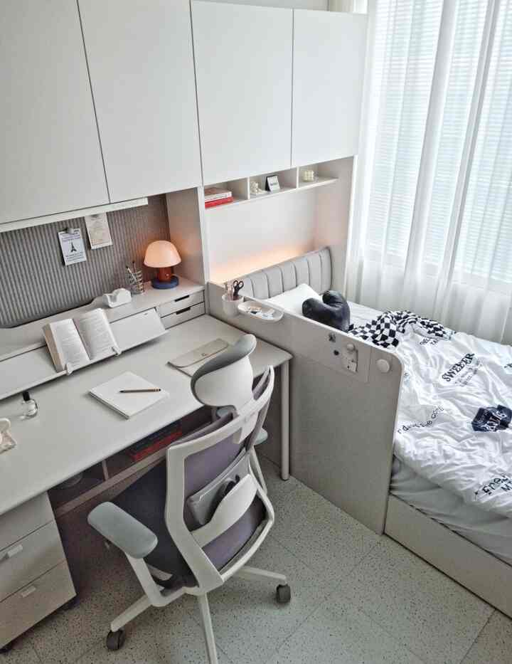 ホワイトトーンのコンパクトな寝室兼ホームオフィス、デスクとベッドが配置された清潔感あるシンプルモダンなインテリア