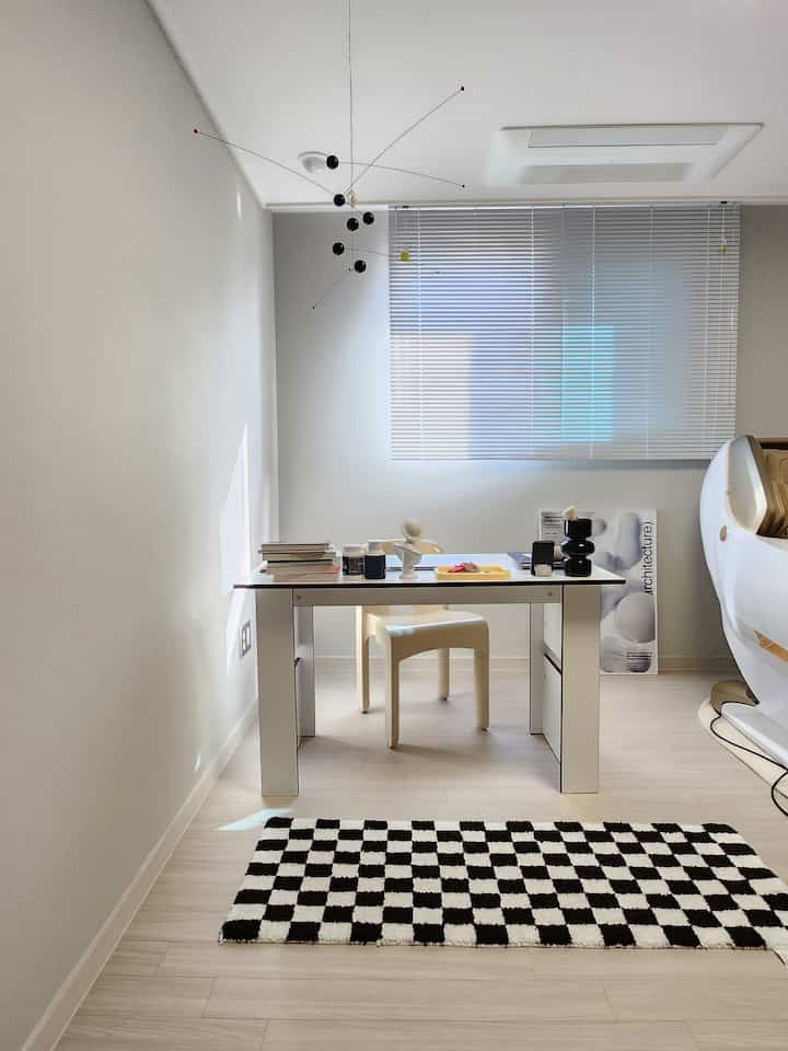 White and black tone study with desk and chair centered, checkerboard rug on floor, creating a modern bright space