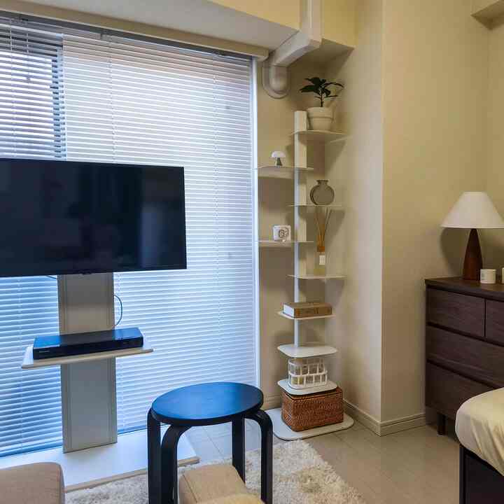 白とナチュラルトーンの1Kリビング、テレビとコーナーシェルフ、モダンで印象的な小さな部屋インテリア