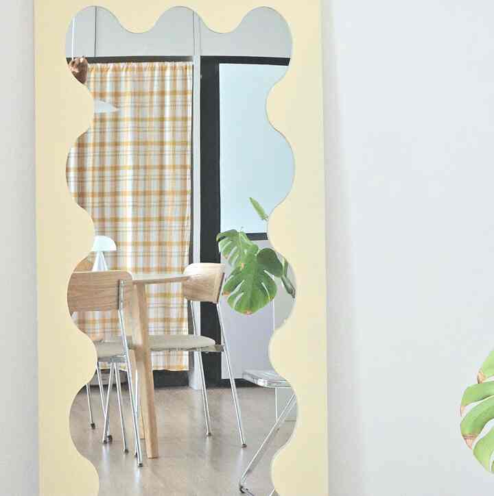 白い壁とベージュの特徴的な波形鏡が配置され、ミッドセンチュリーモダンのダイニングチェアと共に明るくミニマルなダイニング空間