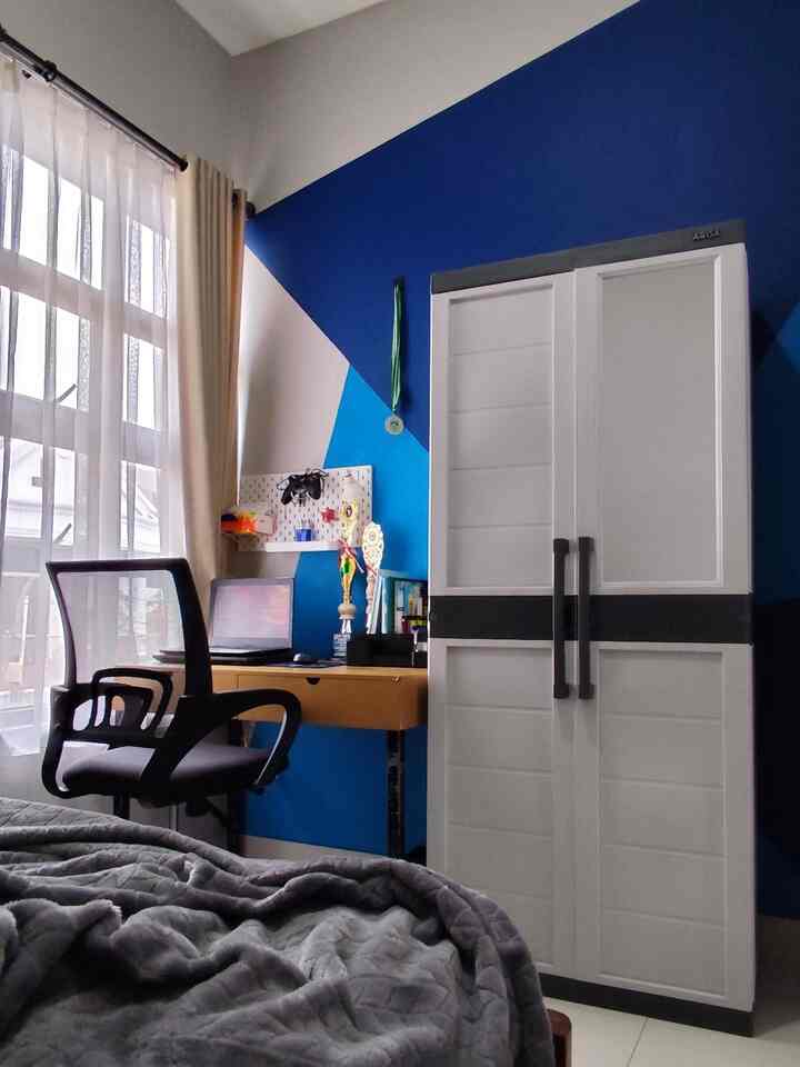 Blue accent wall and ivory curtains define a kids' room with a simple desk and wardrobe creating a neat study space