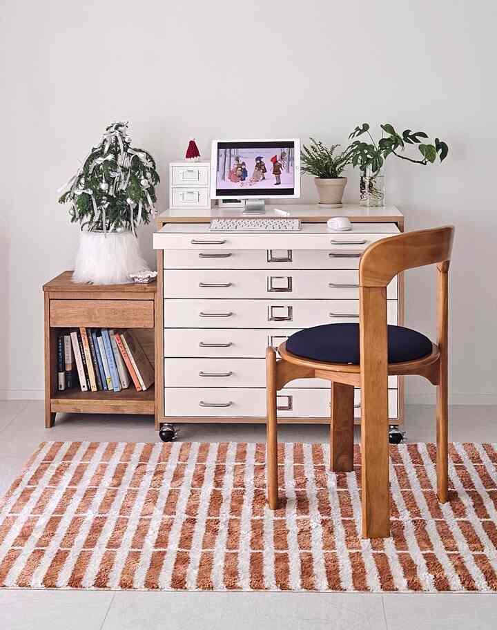 ナチュラルウッドとホワイトトーンの清潔なホームオフィス空間、中央にデスクとモニターが配置され、隣に本棚と植物がある落ち着いたインテリア