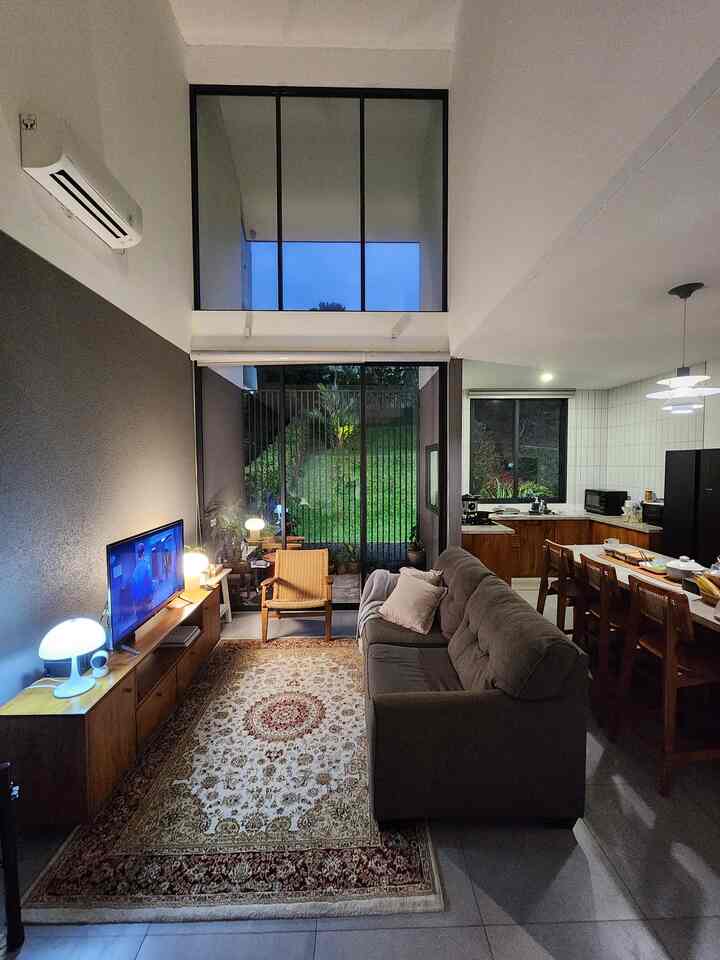A gray and wood tone living room and kitchen featuring high ceilings and large windows, creating a bright and open simple modern interior