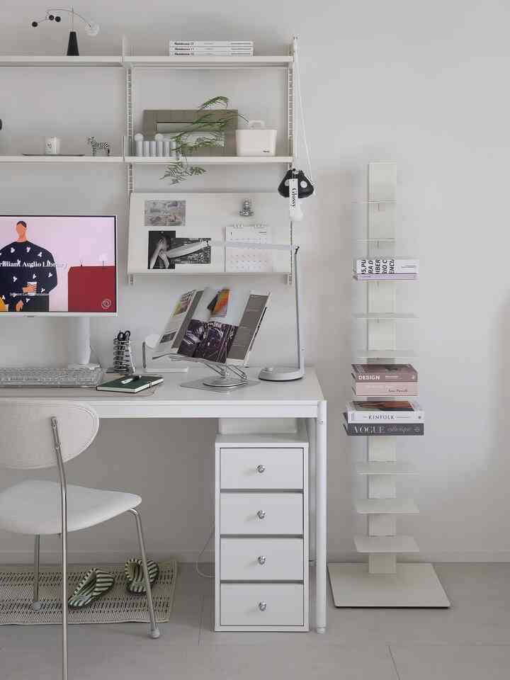 White-toned home office featuring a clean desk, chair, wall shelves, and bookshelf in a simple interior