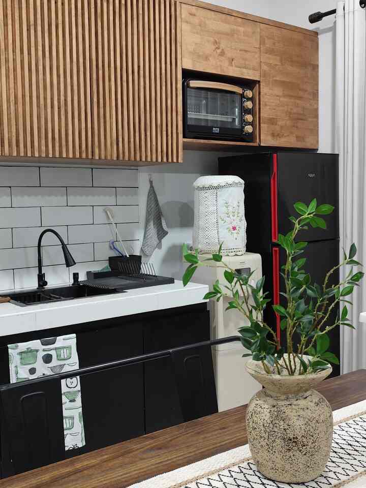 Kitchen featuring wood tone upper cabinets and black lower cabinets, a central sink area, and a green plant on a wooden dining table in the foreground