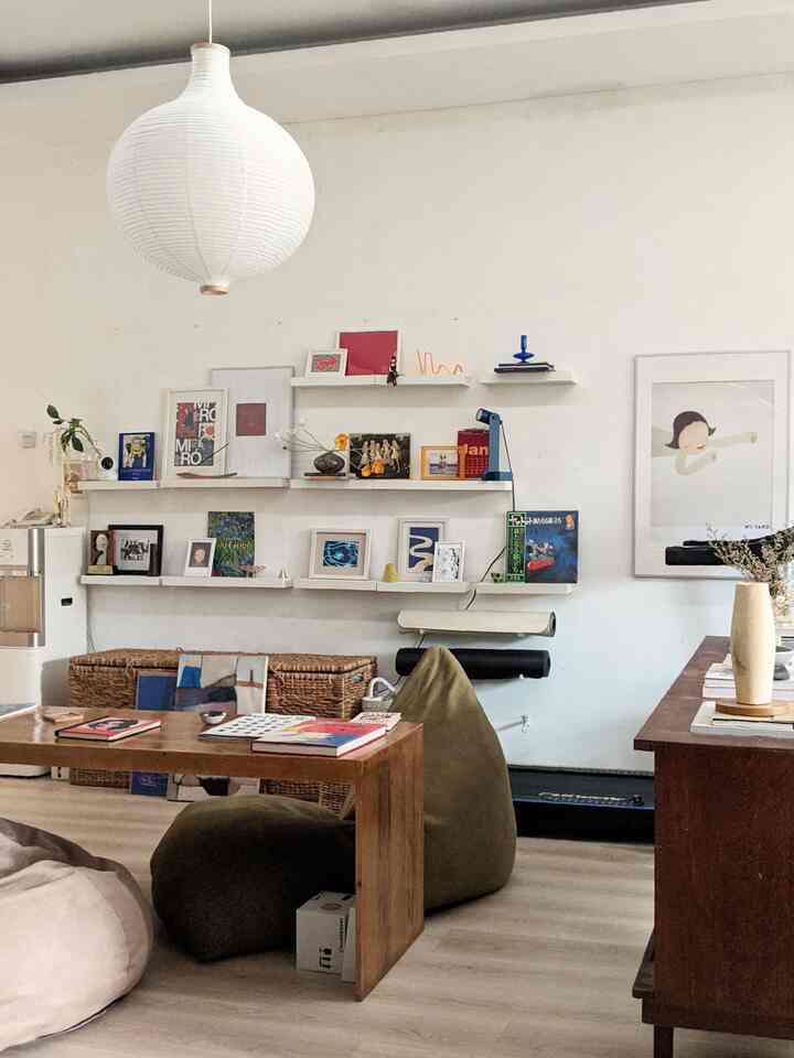 White and light brown toned living room featuring bean bags, wooden table, and wall shelves with various art and decor in a natural, minimal style