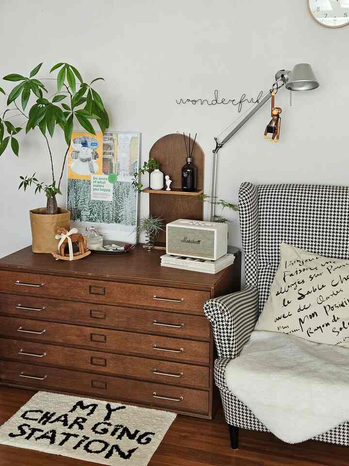 木目調と緑の植物が調和した居心地の良いリビング、ハウンドトゥース柄のアームチェアと多彩なオブジェが配置されたインテリア