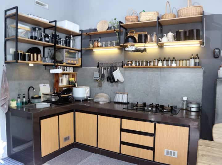 Dapur adalah jantungnya rumah. Semua sumber pangan kita olah disini. Dapur ini kami desain semi industrial dengan rak besi terbuka dan lemari bawah dari kombinasi material alumunium dan pvc yang anti rayap & air. Kombinasi warna kayu terang dan besi hitam memberi kesan hangat namun tegas. Kami sebut dapur ini dapur maksimalis karena mengekspos barang2 di rak terbuka. 
Pemakaian rak terbuka juga lumayan menekan budget pembuatan kitchen set. Pemilihan rak terbuka ini cukup efektif karena tidak perlu repot buka tutup pintu lemari. Namun, kekurangannya rak ini cepat berdebu.  

Dapur ini bersebelahan dengan meja makan. Area ruang makan ini adalah ruang favorit kami karena bersebelahan dengan courtyard / healing garden. Hawa tempat tinggal yang panas menjadi sejuk dengan adanya taman dalam rumah. 
Suasana ruang makan menjadi sangat sejuk ketika sarapan pagi, makan siang ataupun saat ngeteh sore. 

#kitchenset
#kitchensetmaksimalis
#kitchenindustrial
#dapurindustrial
#dapurmodern
#makeoverdapur
#stylingdapur
#dapurimpian