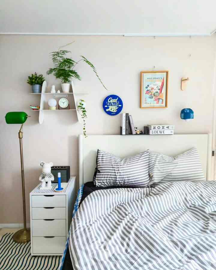 ホワイトとグレーのモノトーンの子供部屋、ストライプの寝具と棚、グリーンのフロアランプが配置された落ち着いた雰囲気のインテリア
