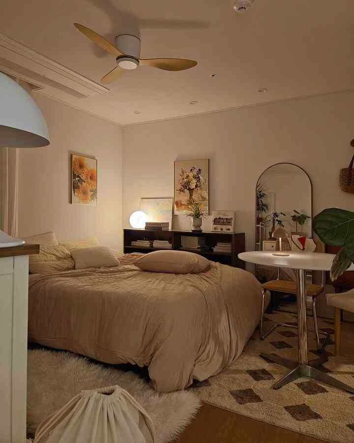 柔らかなベージュトーンの寝室、大きなベッドと丸テーブル、アールデコ風のラグと壁の装飾が温かな雰囲気を醸し出す空間