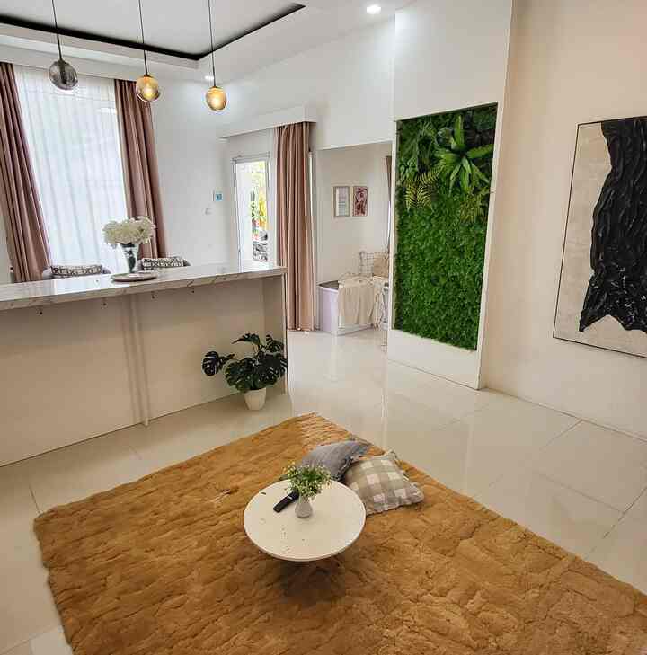 White-toned living room featuring a natural green plant wall, a brown rug with a small round table and cushions creating a cozy atmosphere