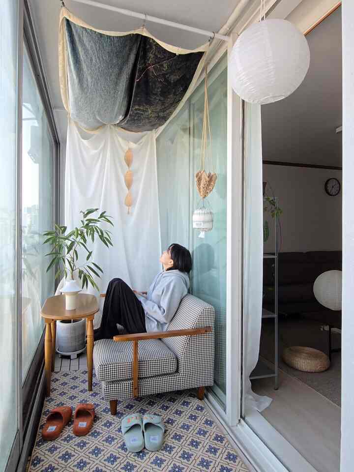 A white and natural tone veranda featuring a vintage patterned rug, sofa, side table, and plants creating a cozy relaxation area