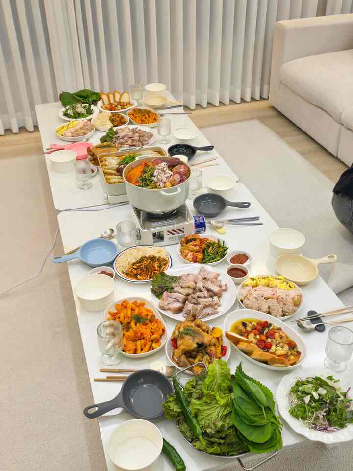 白とベージュのトーンでまとめられたリビング、低いテーブルに多彩なホームパーティー料理と食器が配置された雰囲気のある空間