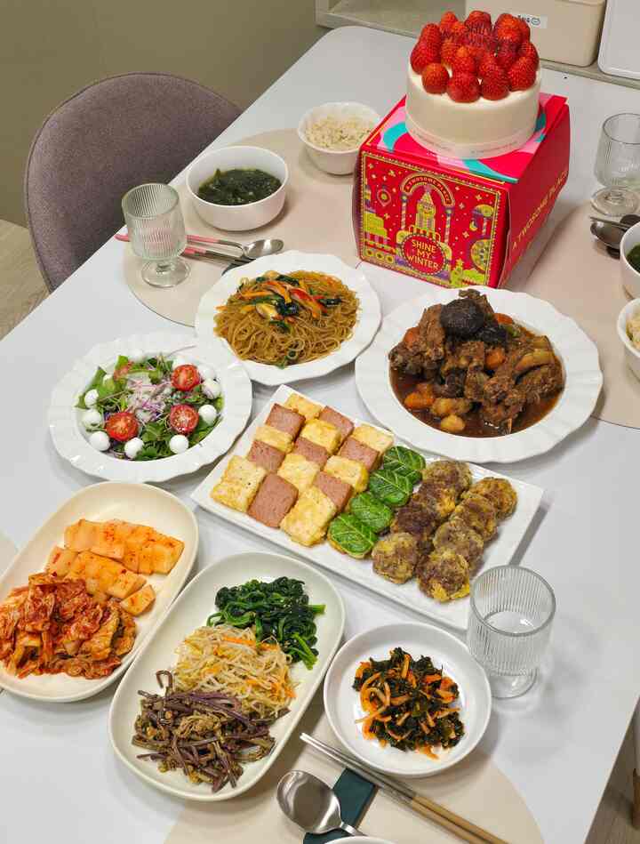 白いダイニングテーブルにベージュのテーブルランナー、多様な韓国料理とケーキが並ぶ4人用のホームパーティー空間