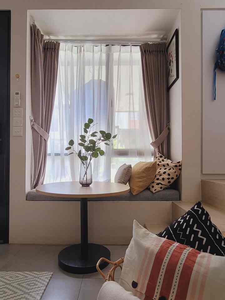Beige and gray toned small room veranda window seat featuring round wooden table and cushions in a cozy cafe-style setting
