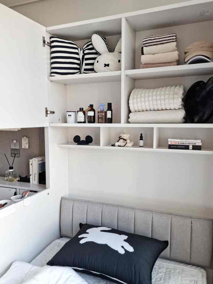 白とグレーのトーンが落ち着くコンパクトな寝室、壁に配置された棚と収納がある清潔感のあるインテリア