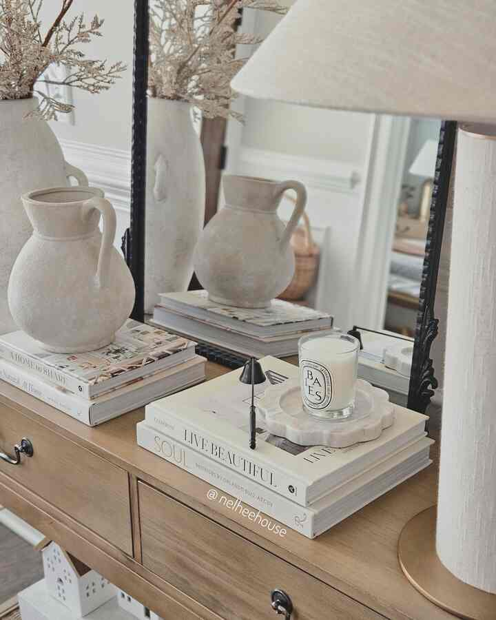 Natural color entrance console table featuring table lamp, vase, candle, and books arranged stylishly in a cozy setting