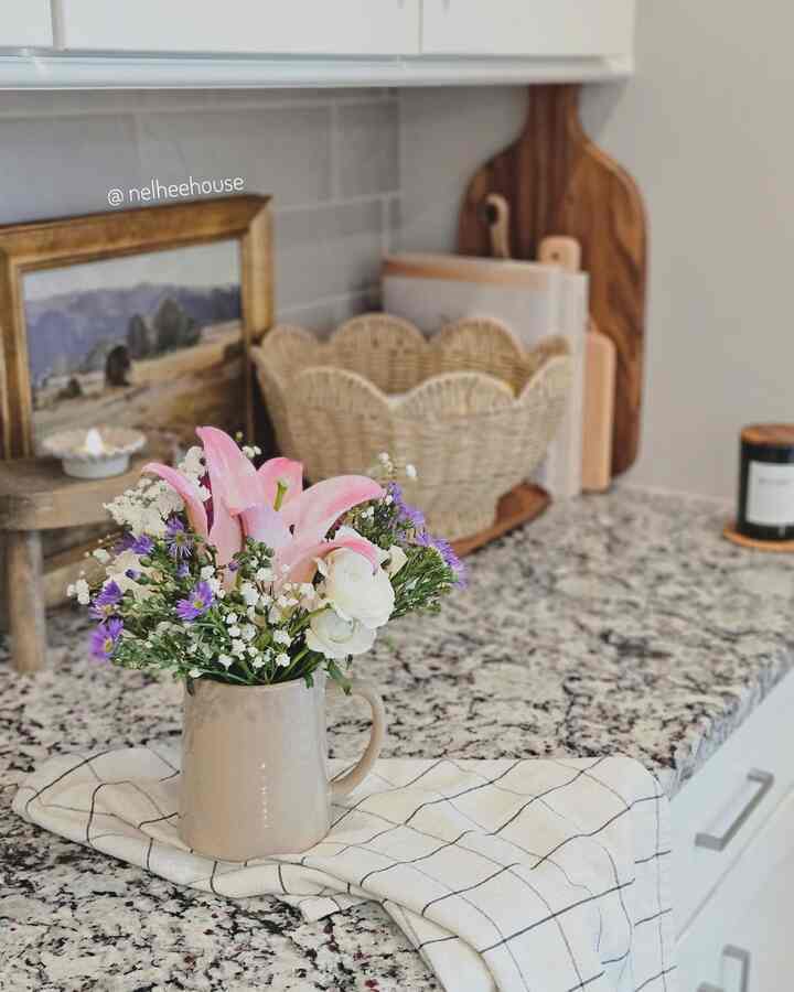Natural-tone kitchen featuring a vase with pink lilies, white and purple flowers on a granite countertop creating a cozy kitchen decor