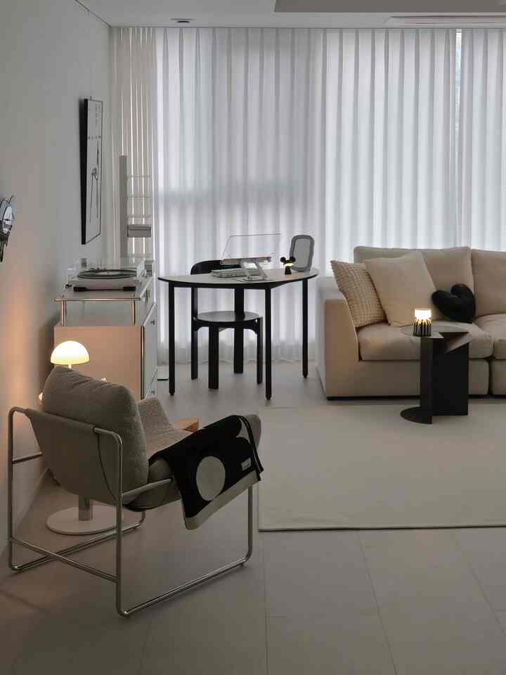 Bright white-toned modern living room featuring a beige sofa, black round table, and minimalist single chair for a clean interior