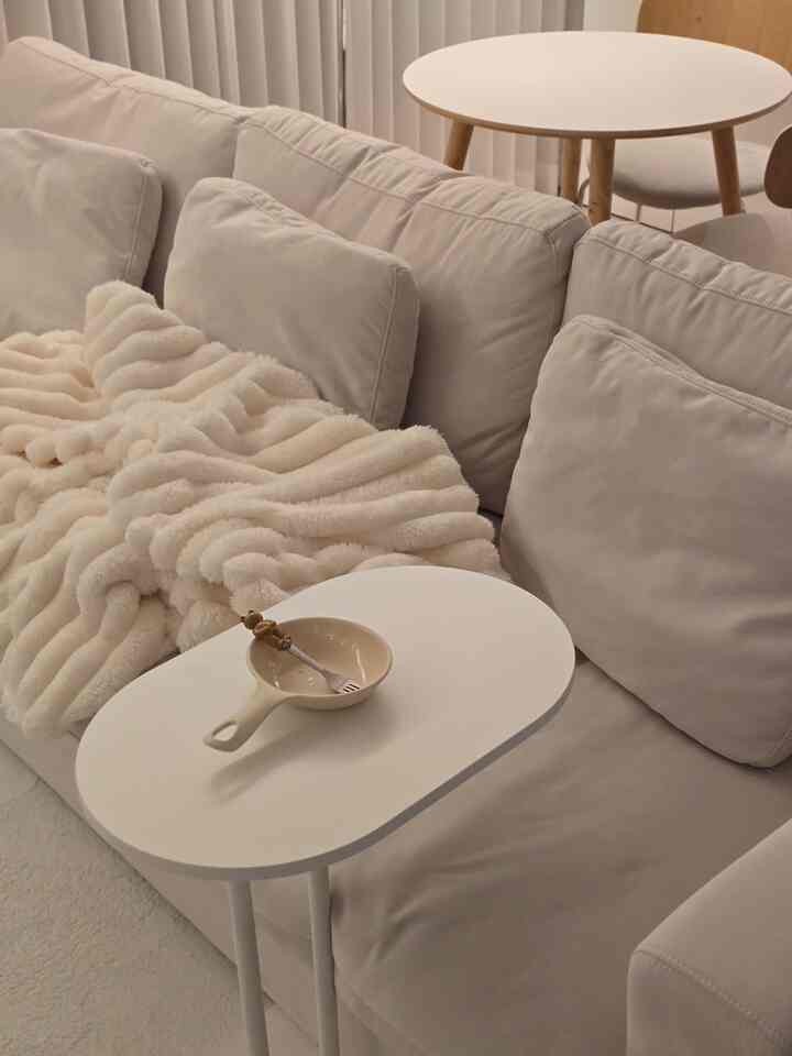 A simple and cozy living room in white and beige tones featuring a cream sofa, small side tables, and a soft blanket