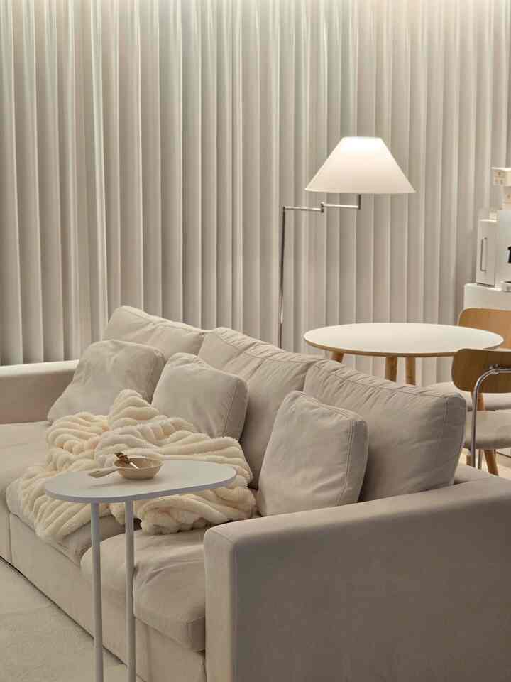 Natural color toned living room featuring a cream sofa, side table, and floor lamp in a cozy, simple setting